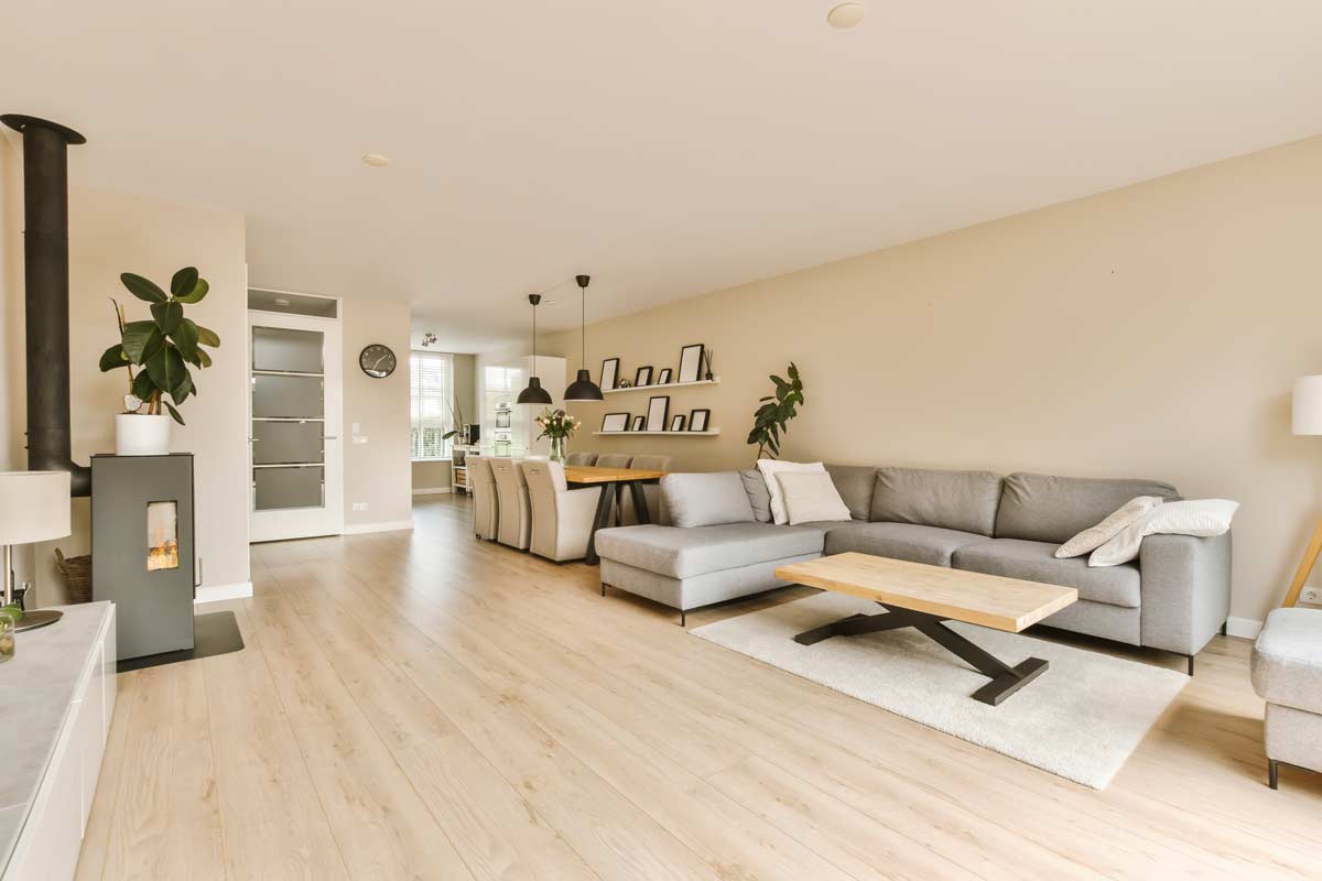 Soggiorno open space moderno con pareti beige, divano grigio e pavimento in legno chiaro, illuminato da luce naturale