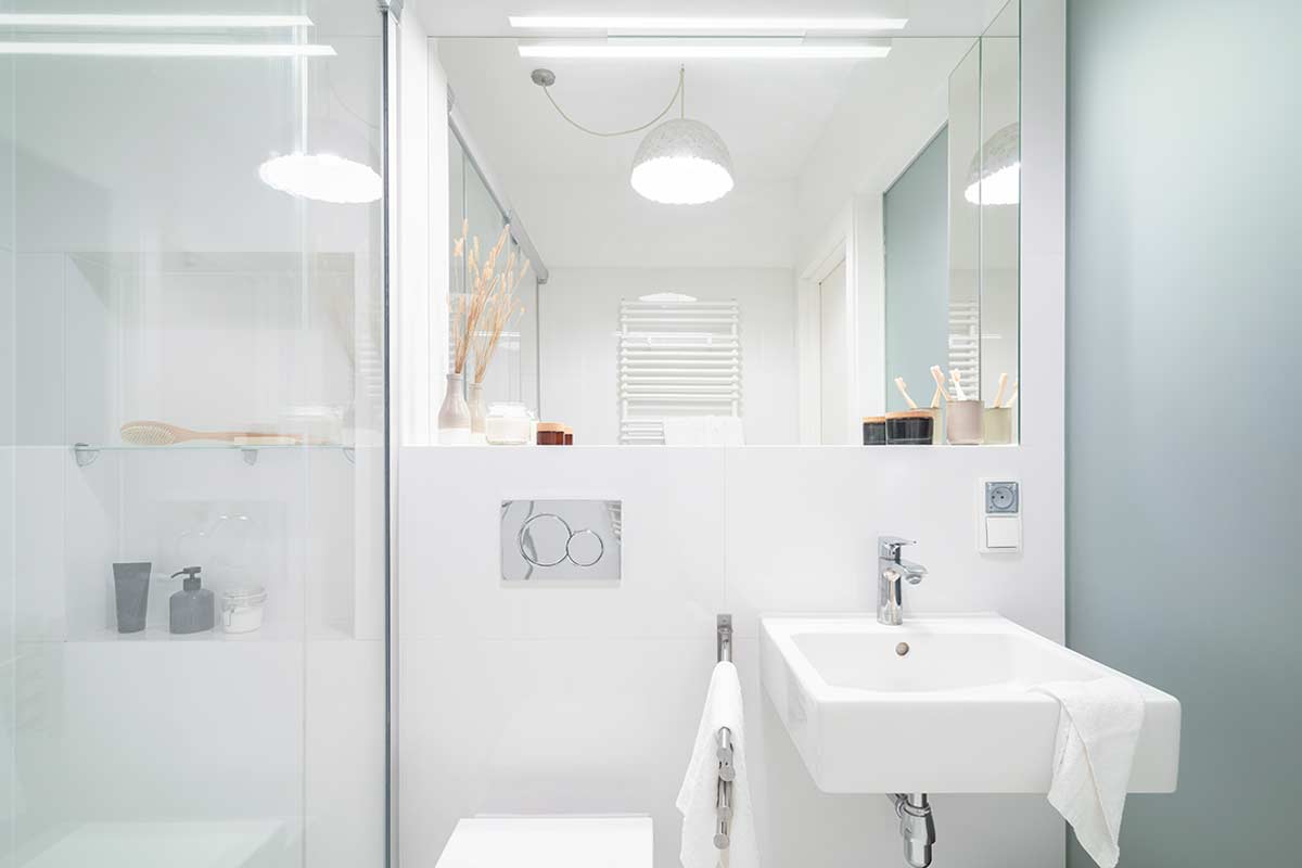 Bagno moderno piccolo tutto bianco con lavabo sospeso, specchio grande, doccia in vetro e dettagli minimal.
