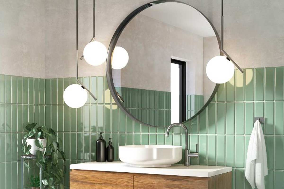 Bagno moderno piccolo con specchio tondo grande, lampade a sfera, piastrelle verde salvia lucide e mobile in legno chiaro.