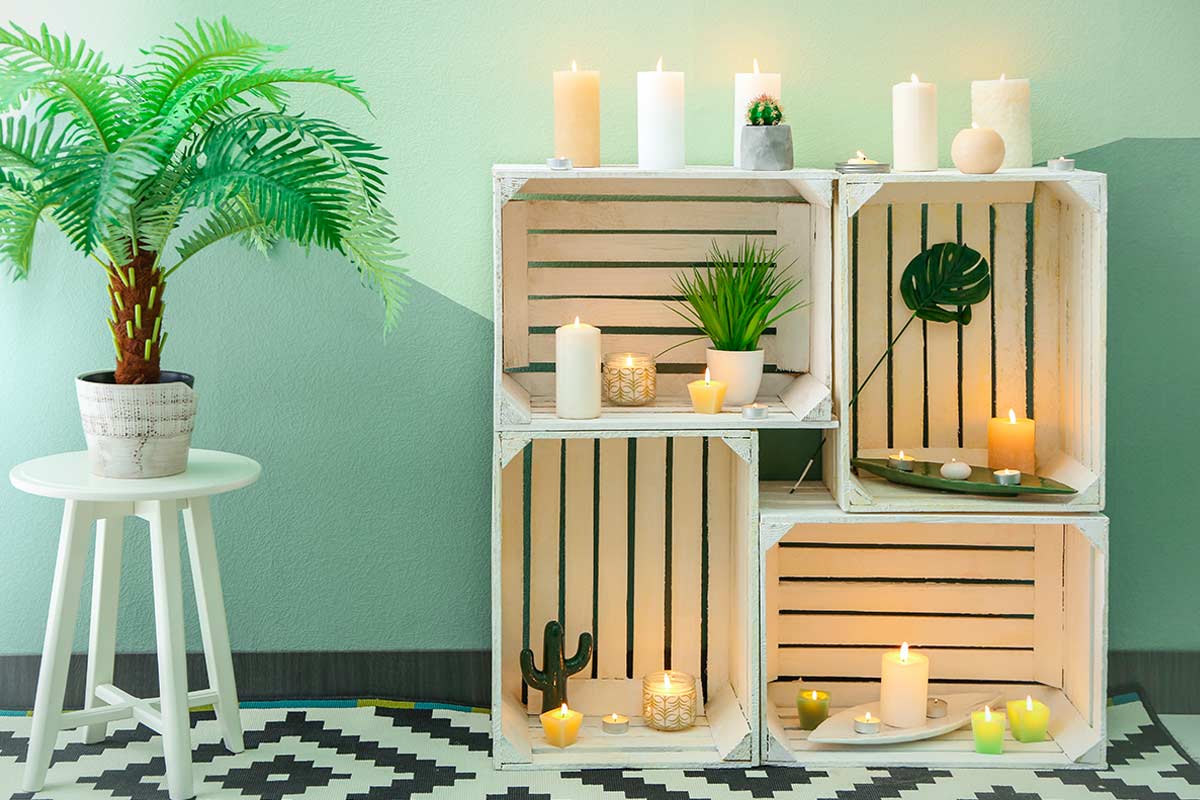 Console bassa realizzata con cassette di legno riciclate, decorata con candele e piante su tappeto geometrico bianco e nero.