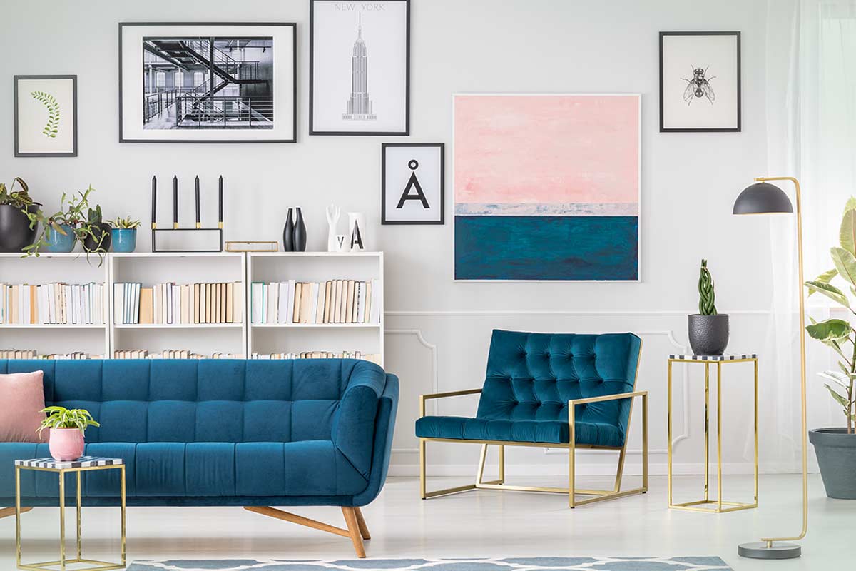 Salotto luminoso con parete decorata da quadri, grande quadro XXL, divano blu e libreria bianca. Atmosfera moderna e accogliente.