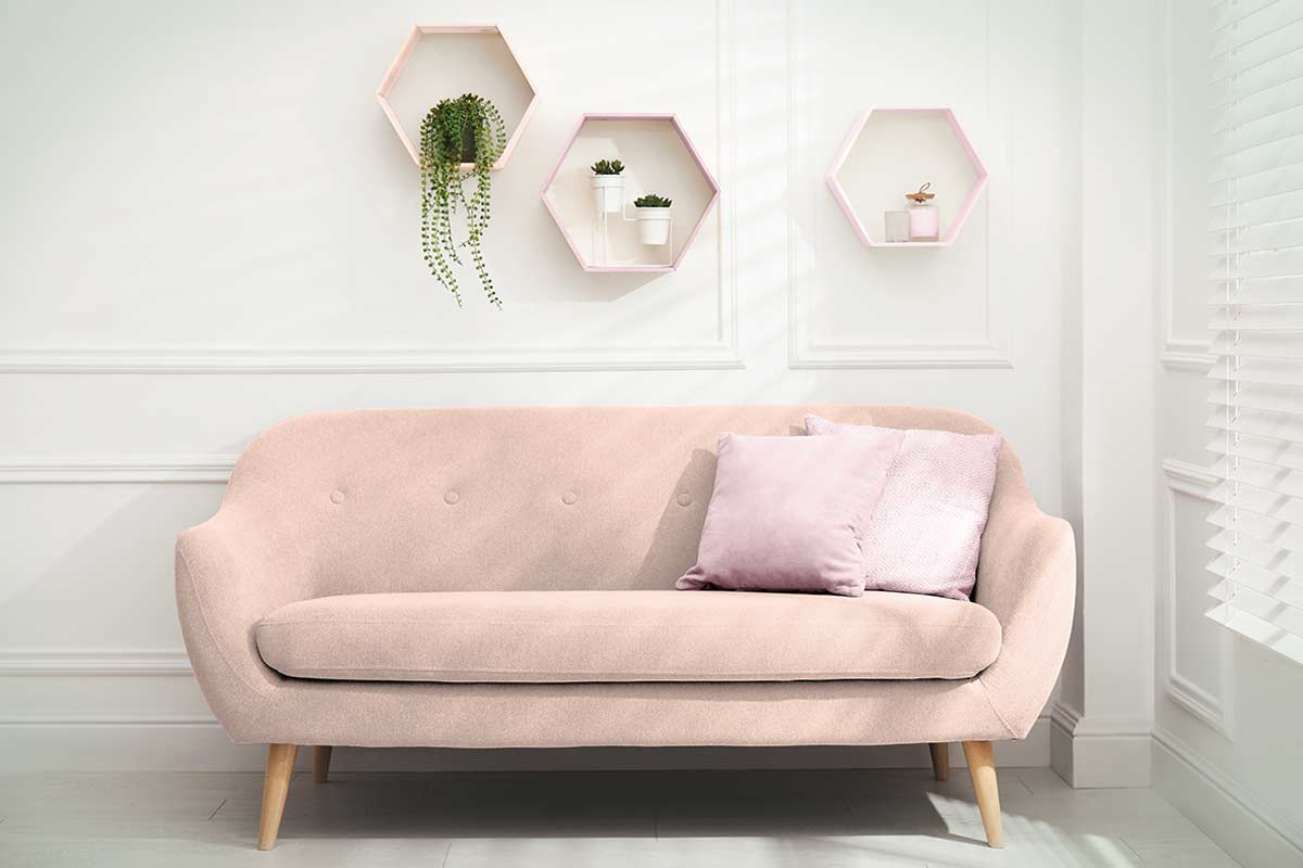 Divanetto rosa chiaro con cuscini, parete decorata da mensole esagonali e piccole piante. Angolo luminoso e delicato.