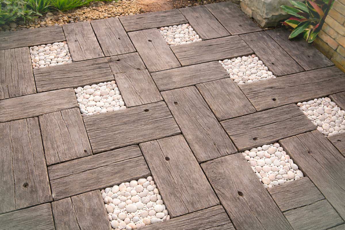 Pavimento esterno fai da te con quadrotti effetto legno alternati a riquadri di ciottoli bianchi, ideale per terrazzi o piccoli giardini.