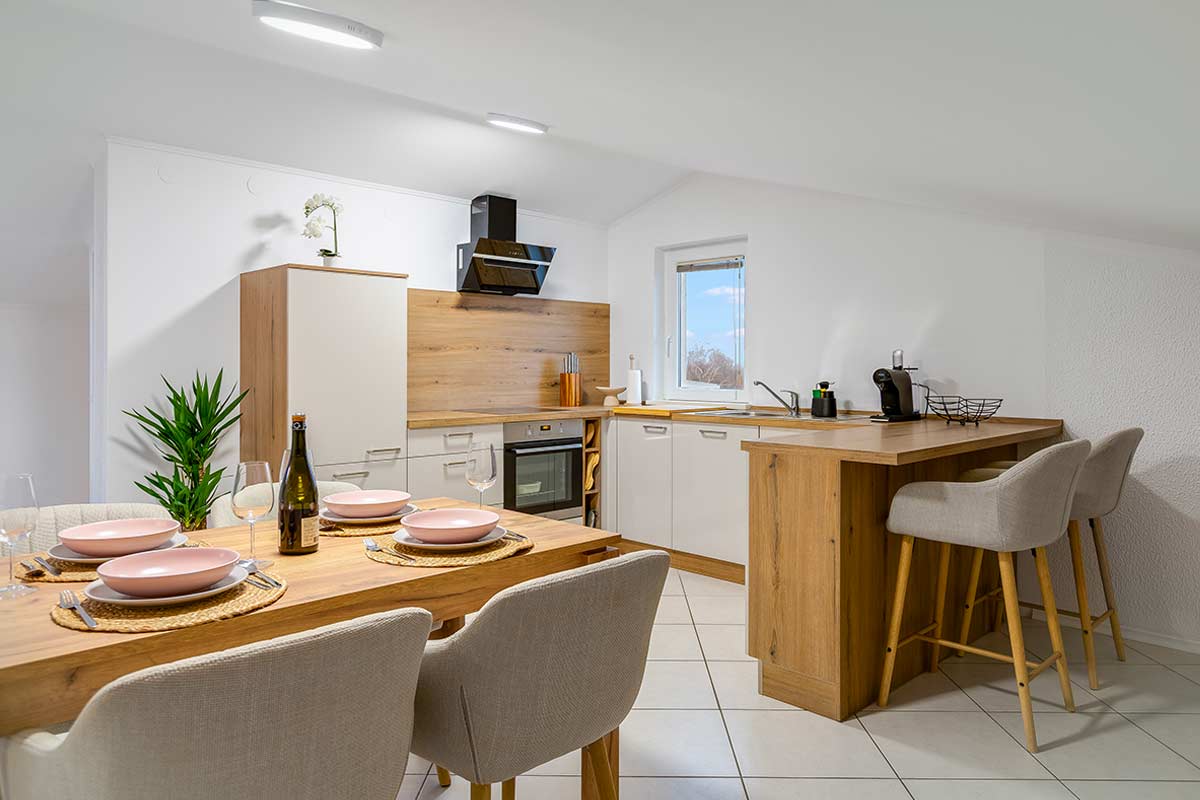 cucina moderna con soffitto basso e arredamento in legno chiaro, tavolo apparecchiato e luce naturale dalla finestra